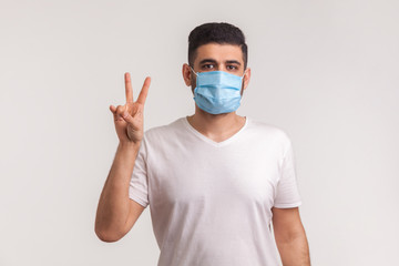 Man flu survivor in hygienic mask showing victory gesture, rejoicing recovery from infection, respiratory illness such as coronavirus, ebola, concept of defeating epidemic. studio shot, isolated