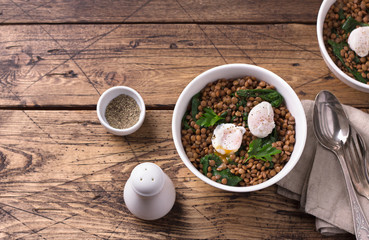 Boiled lentils with spinach, herbs, spices and poached egg in ceramic bowls on a wooden background. Simple healthy homemade food. Top view, space	