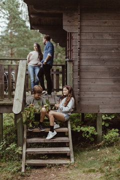 Full length of sibling sitting on steps while parents standing in porch