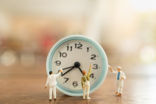 Time management concept. Close up of group of worker miniature people figures clean and paint vintage round clock on wooden table.