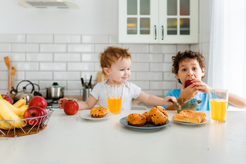 Happy children real brother and sister having breakfast with fruits in bright kitchen at the home