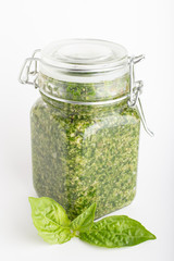 Pesto sauce in a glass jar isolated with fresh basil leaves on white background. Traditional homemade Italian sauce pesto and basil.