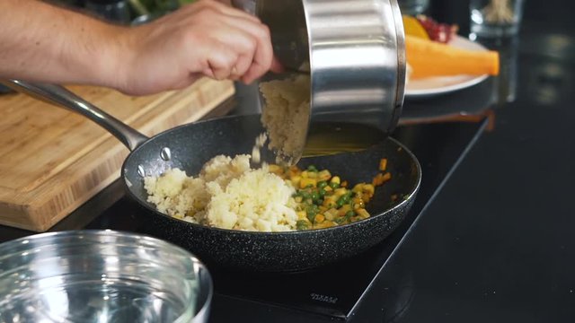 Cook from pan rakes boiled rice into frying pan with vegetables, cooking vegetable pilaf, rice with peas, carrots, corn, cooking, nutrients, mixture, steam, demonstration of cooking, close-up