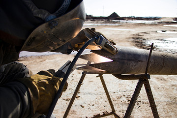 Welder in protective clothing for welding. Pipe preparation for a drilling rig. At the construction site.
