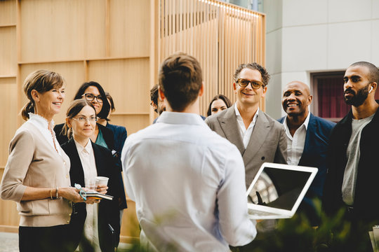Rear view of male professional with laptop talking to colleagues outside office