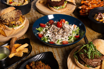 Variety of Mexican-style dishes. Restaurant menu, salad, fried yucca and hamburgers on wooden table.