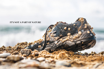 Concept of environmental protection and pollution. An old Shoe covered with shells lies on the seashore. In the background, the sea. The inscription 