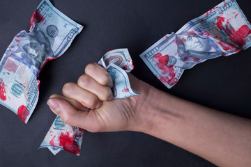 on a black background, close-up hand gripping bloodied dollar bills. Concept