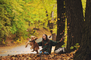 Young woman and her dog (American Cocker Spaniel) sitting in the park and throws up leaves.