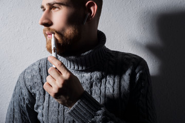 Fototapeta na wymiar close-up. Art portrait of a young bearded guy smoking a modern high-tech electronic cigarette iqos