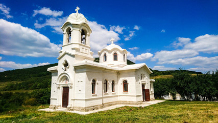 Russian Old ancient stone white church in the green forest, cloudy blue sky