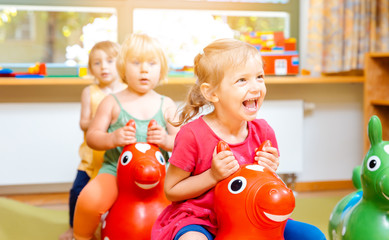 Little girls riding on play horses in kindergarten