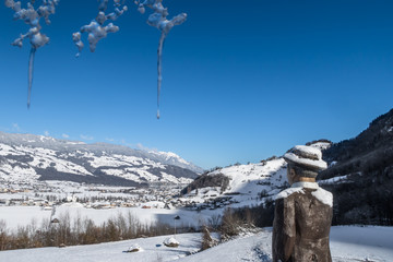 LUNGERN, SWITZERLAND - FEBRUAR 13, 2018: A wooden sculpture of a man watching the winter landscape above the lake Lungern. Icicles above his head.