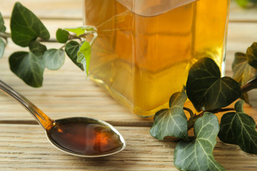 Ivy leaf and syrup in a bottle on a natural wooden table. Production of cough medicine with ivy...