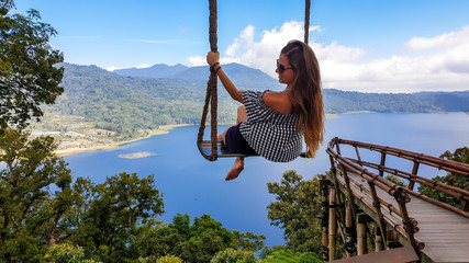 Woman with long hair enjoying her time on the swing with The Twin Lake behind, Bali, Indonesia. The swing is attached to a tree very high above the lake. She is having a lot fun. Touristic attraction