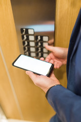 Man hands holding blank screen mobile phone while using elevator control panel.