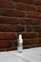 Bottle of serum, hyaluronic acid, botulin on white wooden table. Grunge red brick wall for your logo or text. Side view.