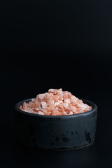 Fototapeta na wymiar Pink Himalayan salt in black ceramic bowl. Black background, high resolution