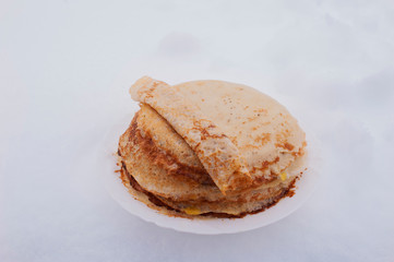 pancakes on a plate are on the snow,thin ruddy pancakes on a plate on a white backgroun