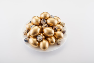 Golden eggs mixed with quail in a plate, on a white background. The concept of Easter, a symbol of the holiday, abundance and wealth.