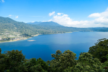 Fototapeta na wymiar A panoramic view on The Twin Lake, Bali, Indonesia. The lake is surrounded by lush green plants. There are small hills all around the lake. Touristic attraction. Biggest lake on Bali