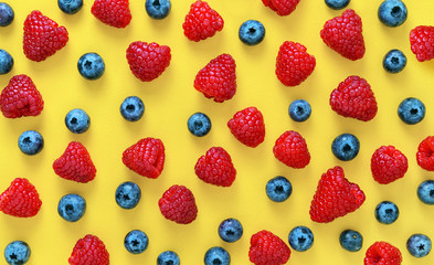 Colorful fruit pattern of raspberries and blueberries on yellow background. Flat lay
