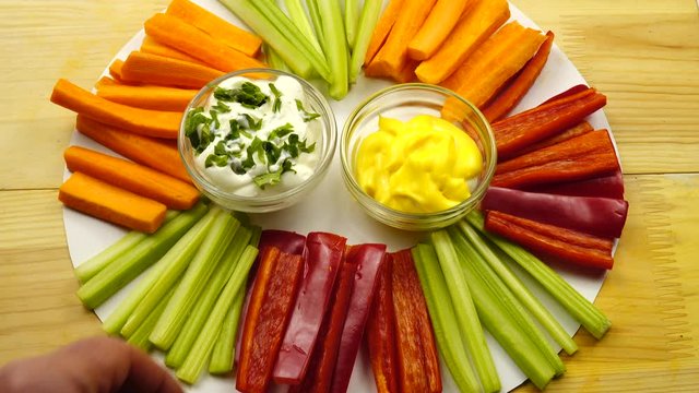 A slice of red sweet pointed pepper is dipped in white vegan sauce, vegan snack