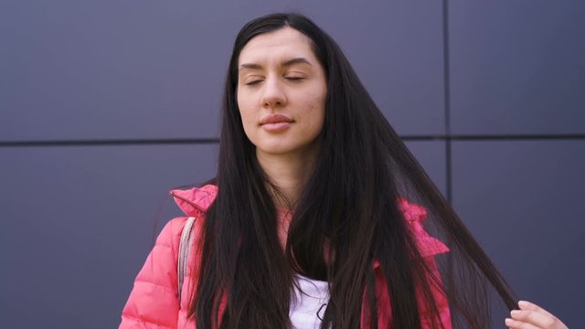 Thoughtful young woman playing with her long hair dressed in pink jacket