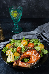 Grilled red fish steak, salmon, salmon with fresh salad of greens and cherry tomatoes on a black background.