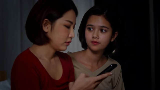 4K Young beautiful Asian woman comforting her sad friend that get bad news from smartphone. Woman hugging and consoling her depressed girls friend at night. Teenage problems and friendship concept.