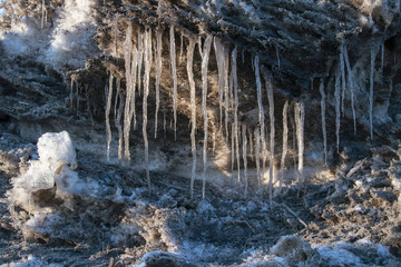 Icicle, dirty ice stalactite sharpened downward when melting dirty snow on a rocky ledge.