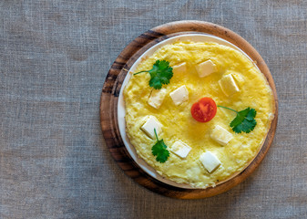 Omelet with feta cheese and vegetables on white and wooden plate with gray linen textured background