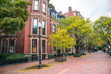 Historic residential buildings along a tree lined sidewalk on an overcast fall day. Boston, MA, USA.