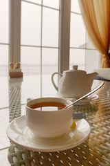 One hot tea white cup on rattan table in hotel restaurant. Tea with lemon for breakfast at a cafe in the resort. Morning tea cup with teapot on table in country house