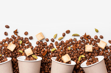 Roasted coffee beans, cane sugar, cardamom, star anise and paper cups on a white background top view, copy space, flat lay. Coffee takeaway concept. Coffee with spices.
