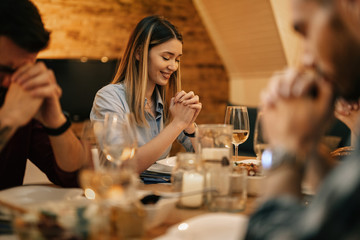 Smiling woman say grace while having dinner with friends in dining room.