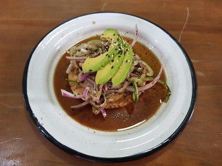 In a seafood restaurant eating a black Aguachile toast with avocado