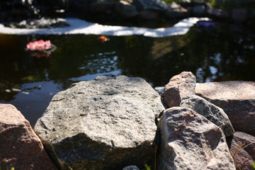  waterfall in its own courtyard in the summer against the backdrop of nature where pink lily blooms around and stones