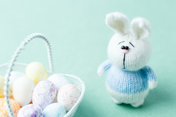 Easter concept. Knitted bunny staying near basket with eggs