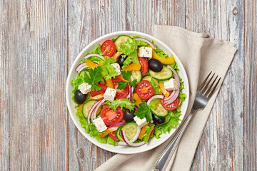 Greek salad with cucumeber, olives, feta cheese, cherry tomatoes, bell pepper, onion and lettuce. Diet, vitamin food. Healthy vegetarian meal concept. Tasty salad in bowl on wood, top view.