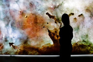 Young woman standing in front of the huge picture of star nebula. Woman in the universe. Woman...