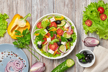 Greek salad with cucumeber, olives, feta cheese, cherry tomatoes, bell pepper, onion and lettuce. Diet, vitamin food. Healthy vegetarian meal concept. Tasty salad in bowl on wood, top view.