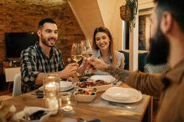 Young happy friends toasting with wine during dinner in dining room.