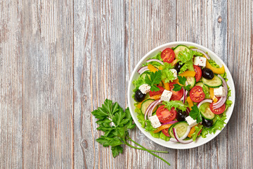 Greek salad with cucumeber, olives, feta cheese, cherry tomatoes, bell pepper, onion and lettuce. Diet, vitamin food. Healthy vegetarian meal concept. Tasty salad in bowl on wood, top view. Copy space