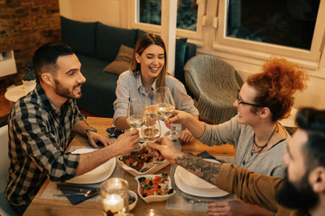 Above view of young happy people toasting at dining table.