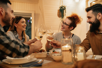 Group of cheerful friends toasting with wine at dining table.