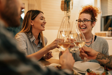 Cheerful women and their friends having fun while toasting at dining table.