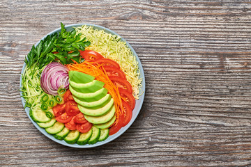 Fresh salad with avocado, lettuce, cucumber, cabbage, carrot, onion. Diet, healthy vegan salad, balanced food concept. Buddha bowl mix vegetable homemade salad on wood, top view. Copy space