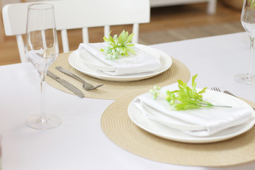 .Plates with twigs of artificial flowers on beige round napkins, glasses and cutlery on a white table..Festive table setting for two persons..