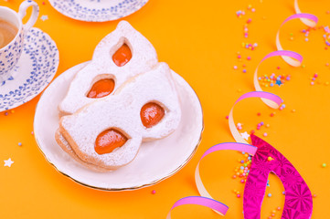 Cookies with powdered sugar in the form of a carnival mask and espresso on a yellow background. Festive decor and sweets. Free space for text.
